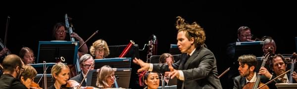 A conductor waves his arms enthusiastically before an orchestra