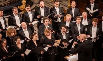 A choir dressed in formal wear sings in front of their conductor.