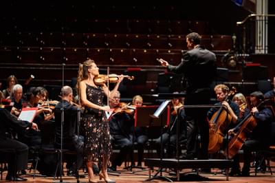 A woman stands on stage playing a violin