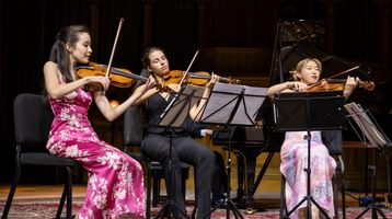 Three women seated on stage playing string instruments