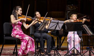 Three women seated on stage playing string instruments