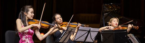 Three women seated on stage playing string instruments