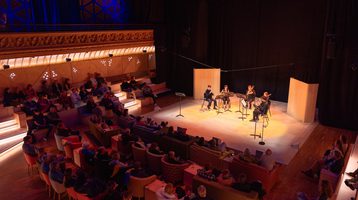 Five musicians playing on a warmly lit stage to an audience.