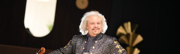 A man is standing smiling with his violin at his side