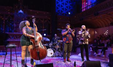 A woman playing the double bass performing on stage with two brass players and a drummer