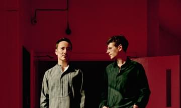 two men stand next to each other with a red background