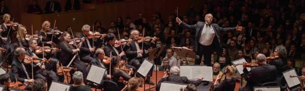 A conductor stands with his arms outstretched in the midst of an orchestra