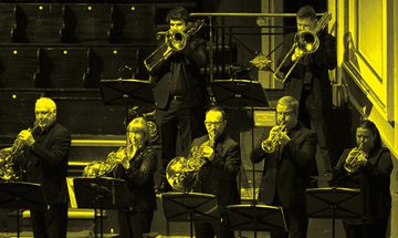 A black and yellow image of a brass ensemble performing on stage