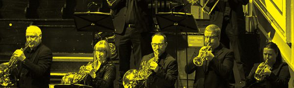 A black and yellow image of a brass ensemble performing on stage