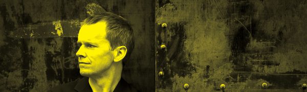 A black and yellow image of Steven Osborne leaning against a wall and looking away from the camera