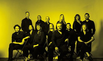A black and yellow image of the Colin Currie Group dressed in black, looking at the camera