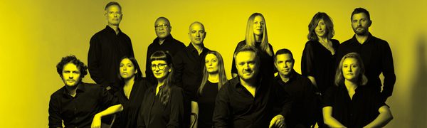 A black and yellow image of the Colin Currie Group dressed in black, looking at the camera