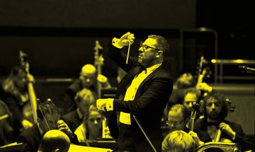 A black and yellow image of a conductor holding a baton and standing in front of the orchestra