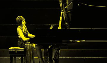 A black and yellow image of Yuja Wang playing piano on stage