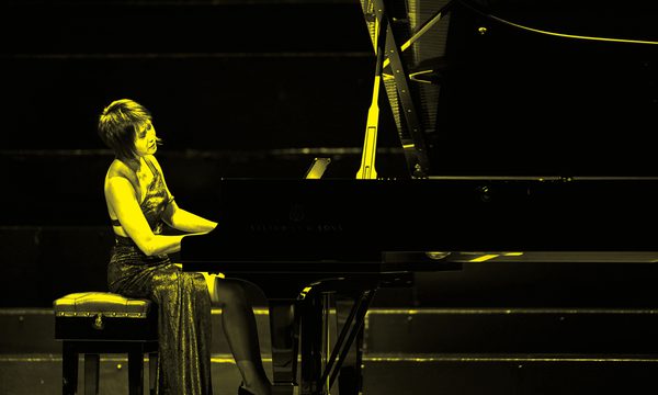 A black and yellow image of Yuja Wang playing piano on stage