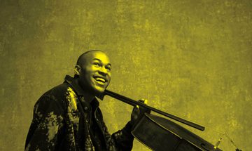 A black and yellow image of Sheku Kanneh Mason holding a cello and smiling