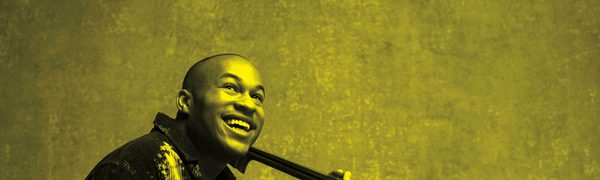 A black and yellow image of Sheku Kanneh Mason holding a cello and smiling