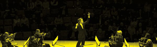 A black and yellow image of a conductor and an orchestra performing on stage
