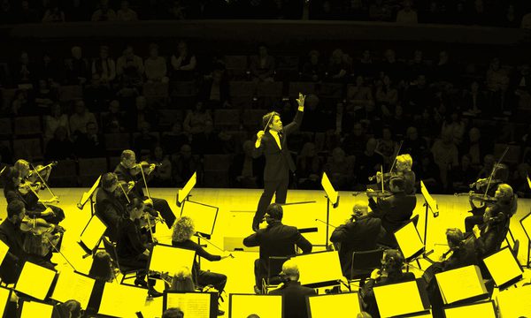 A black and yellow image of a conductor and an orchestra performing on stage