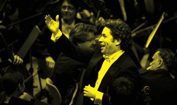 A black and yellow image of a conductor standing in front of an orchestra with his arm in the air while smiling