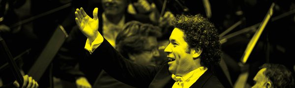 A black and yellow image of a conductor standing in front of an orchestra with his arm in the air while smiling