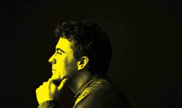 A black and yellow image of Paul Lewis looking away from the camera with a thoughtful expression