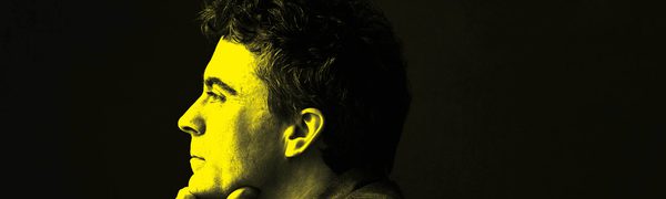 A black and yellow image of Paul Lewis looking away from the camera with a thoughtful expression