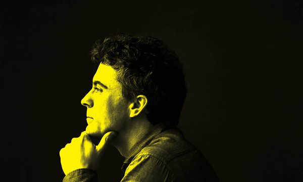 A black and yellow image of Paul Lewis looking away from the camera with a thoughtful expression