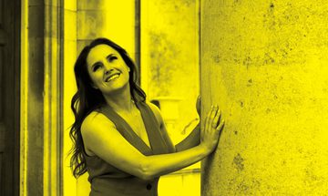 A black and yellow image of Louise Alder leaning against a wall and smiling