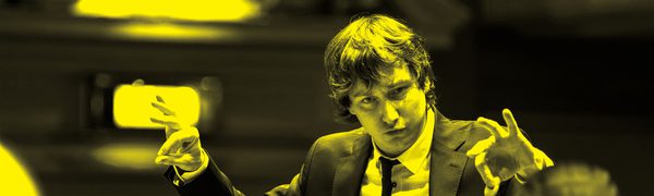 A black and yellow image of Maxim Emelyanychev conducting an orchestra