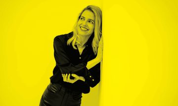A black and yellow image of a woman leaning against a wall and smiling