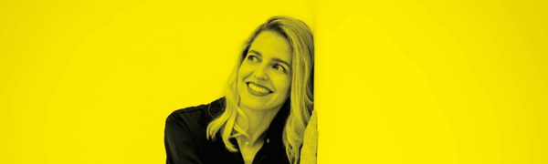A black and yellow image of a woman leaning against a wall and smiling