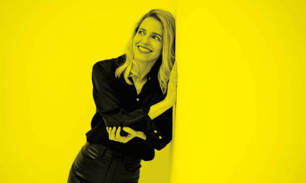 A black and yellow image of a woman leaning against a wall and smiling