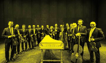 A black and yellow image of the Venice Baroque Orchestra standing in a row holding their instruments