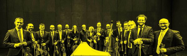 A black and yellow image of the Venice Baroque Orchestra standing in a row holding their instruments