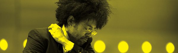 A black and yellow image of Rafael Payare conducting an orchestra while holding a baton and swinging his arm