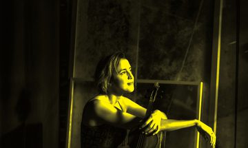 A black and yellow image of a woman sitting holding a violin while looking away from the camera