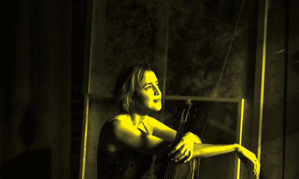A black and yellow image of a woman sitting holding a violin while looking away from the camera
