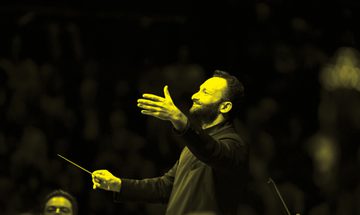 A black and yellow image of a conductor waving his baton and smiling upwards