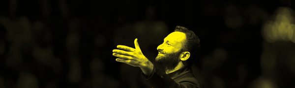 A black and yellow image of a conductor waving his baton and smiling upwards