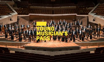 A yellow Young Musicians Pass logo in front of the Berlin Philharmoniker standing on stage