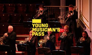 A yellow Young Musician's Pass logo in front of a group of brass musicians stand on stage