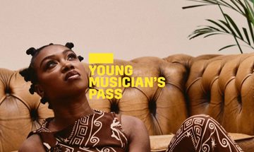 A yellow Young Musician's Pass logo in front of a woman sitting on the floor holding a saxophone and looking upwards