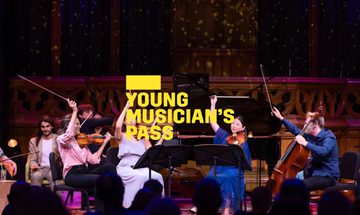 A yellow Young Musician's Pass logo in front of a group of string musicians on stage, holding their bows in the air