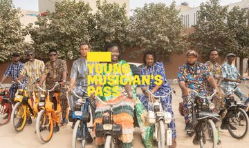A yellow Young Musician's Pass logo in front of a group of people in colourful clothes sit on bikes smiling