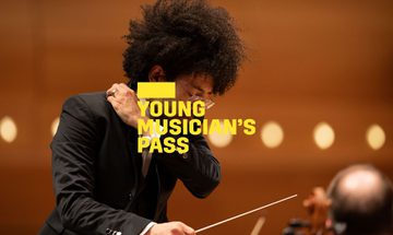 A yellow Young Musician's Pass logo in front of a conductor mid movement
