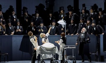 An early 20th century surgeon operates on someone in the middle of a crowded theatre. He holds up a piece of viscera in tongs to the shock of onlookers.