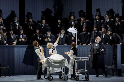 An early 20th century surgeon operates on someone in the middle of a crowded theatre. He holds up a piece of viscera in tongs to the shock of onlookers.