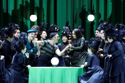 A fortune teller reads the palm of a man dressed like a sailor. Surrounding them are women in black, early 20th century outfits with feathered top-hats.