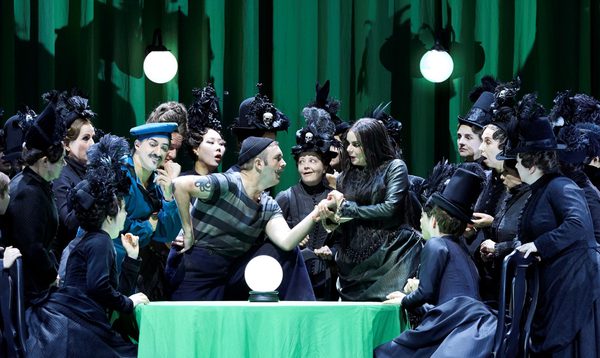 A fortune teller reads the palm of a man dressed like a sailor. Surrounding them are women in black, early 20th century outfits with feathered top-hats.